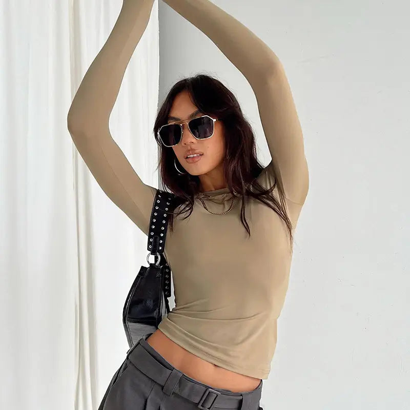 Bolso de hombro negro con tachuelas y acabado brillante, con herrajes plateados, que complementa una blusa corta ajustada tipo slim fit para mujer, con mangas largas fruncidas.