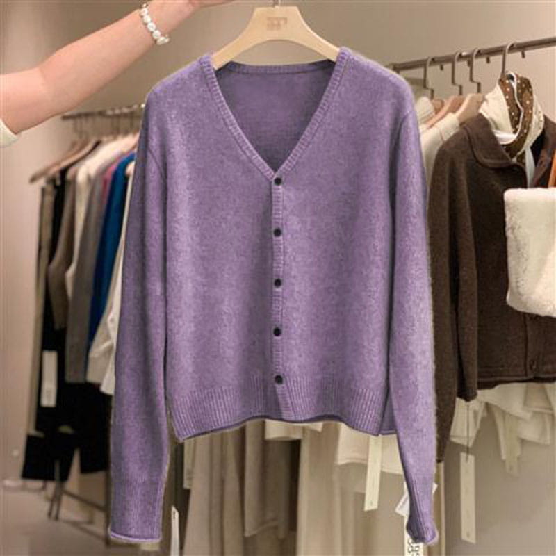 Un pull cardigan en laine mérinos lavande douce à encolure en V, avec fermeture boutonnée, suspendu à un cintre en bois.