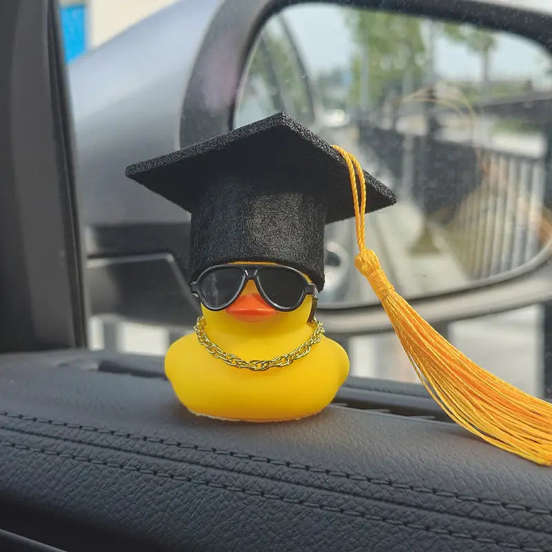 Yellow rubber graduation rubber duck dashboard ornament wearing a black graduation cap with a gold tassel, sunglasses, and a gold chain necklace.