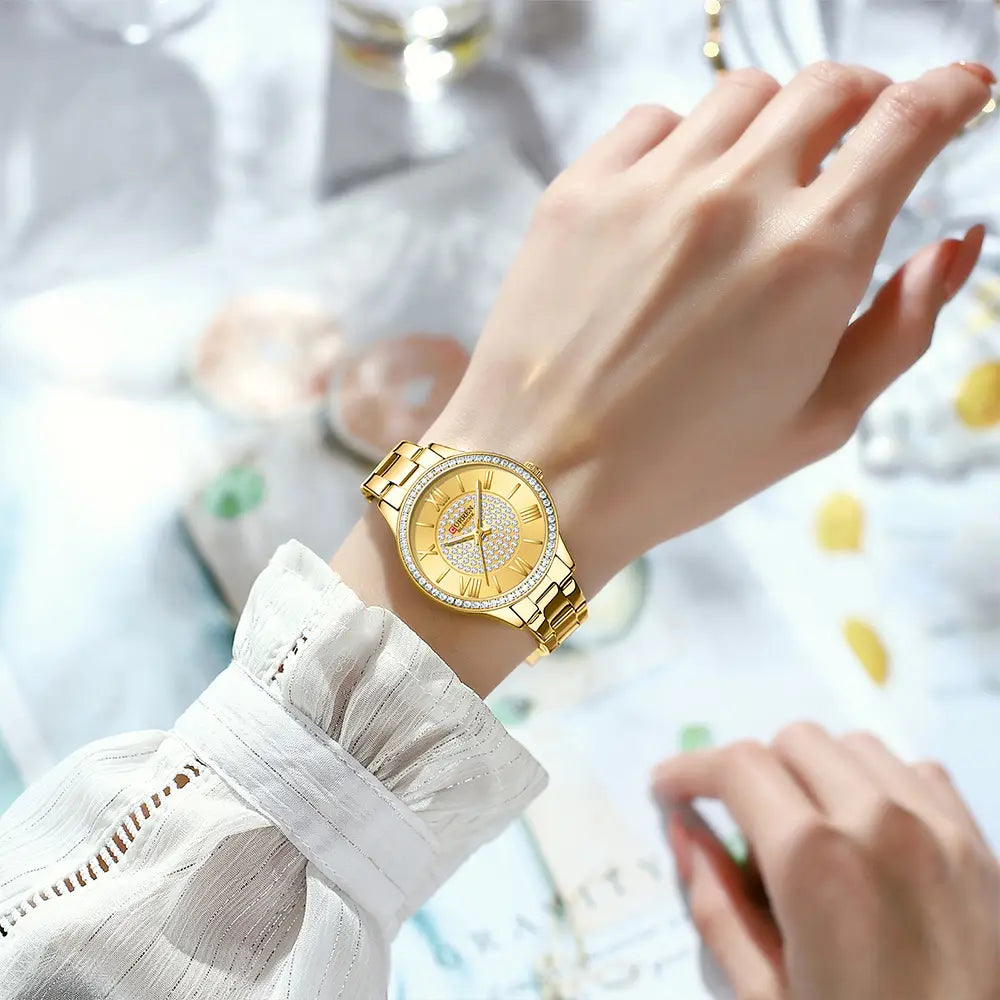 Curren women stainless steel quartz watch in gold tone with diamond-studded bezel and face featuring roman numerals on the dial.