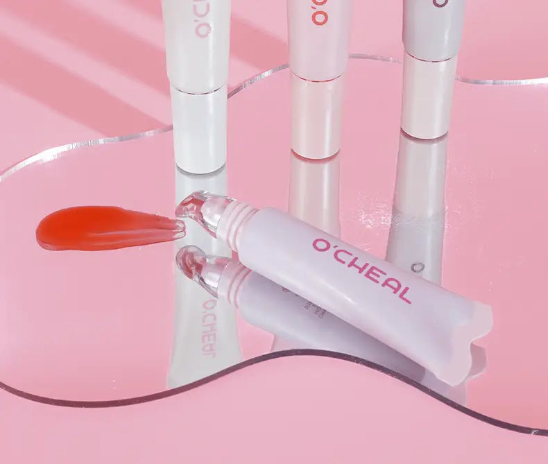 A white o cheal eye serum tube with a clear glass rollerball applicator beside red liquid spilled next to hydrating fruit flavored glossy lip balm.