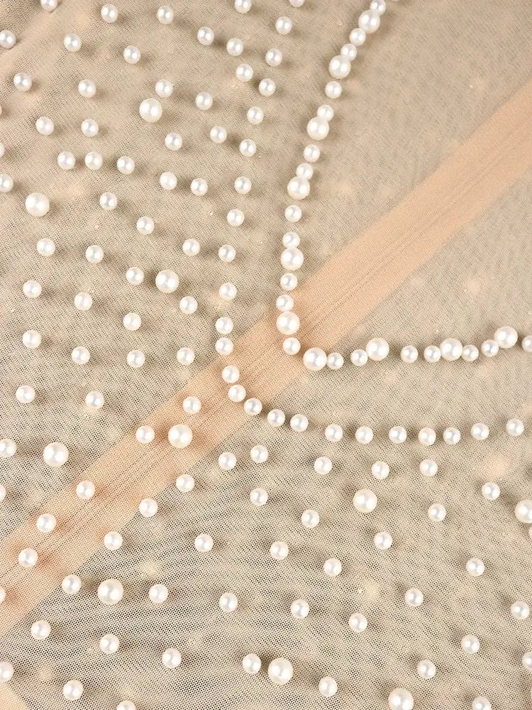 A delicate beige mesh fabric beaded high waisted jumpsuit adorned with evenly spaced white pearls in a subtle geometric pattern for elegant party wear.
