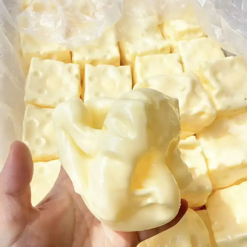 Das Käse-Soft-Glücksbringer-Spielzeug zur Stressreduktion ist ein cremig-weißes, bonbonförmiges Spielzeug mit glatter, glänzender Oberfläche und kleinen Löchern, die wie Schweizer Käse wirken.