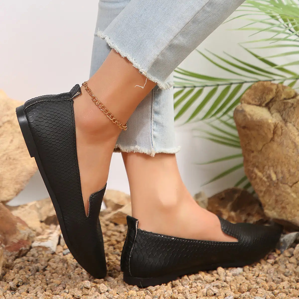 Mocasines planos de cuero negro con textura de piel de serpiente, punta afilada, diseñados para ofrecer comodidad al ponerse y quitarse con facilidad.