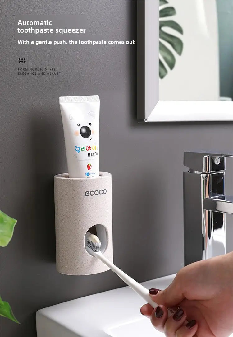 Beige ceramic automatic wall mounted toothpaste dispenser and holder set with ecoco branding holding a white cartoon-themed tube.