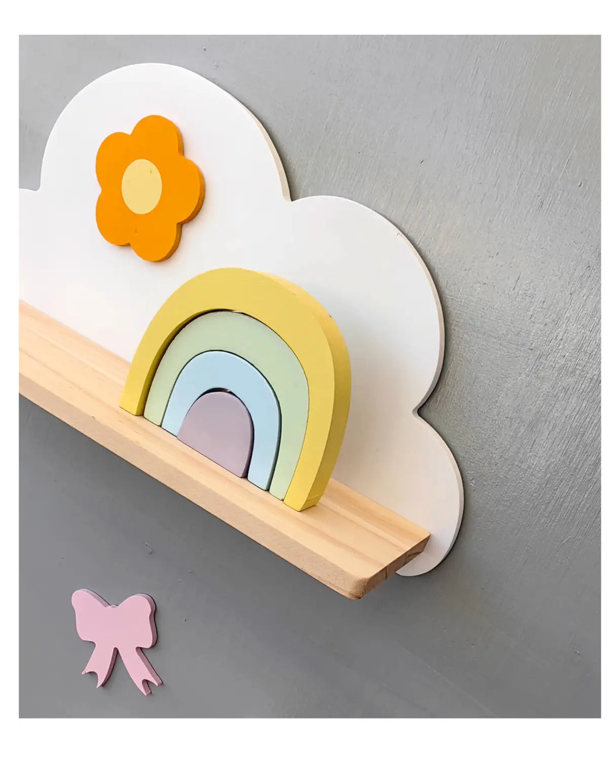 Ein Regenbogen-Wolken-Bücherregal aus Holz für Kinder an der Wand mit einer pastellfarbenen, regenbogenförmigen Holzablage mit geschichteten Bögen und einer Wolkenrückwand mit einer orangefarbenen Blume.