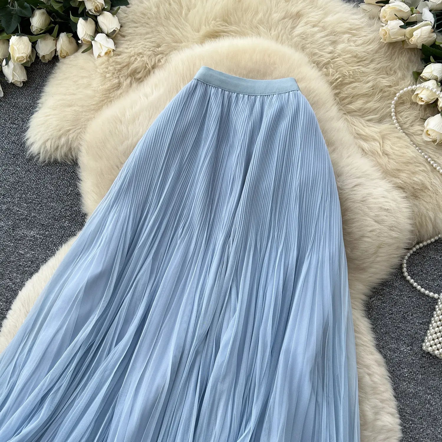Ein fließender hellblauer transparenter Chiffon-Plisseerock Midi mit A-Linien-Design, dargestellt auf einer weichen weißen Felloberfläche für Y2K-Streetwear.