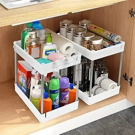 Organizador blanco de almacenamiento bajo el fregadero, de dos niveles y con ruedas, con paneles laterales transparentes y bastidor metálico, diseñado como una estantería multifuncional tipo cajón por niveles para uso en la cocina.