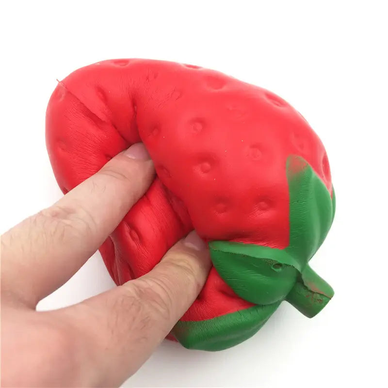 Un juguete antiestrés de fresa gigante roja, que se eleva lentamente y es blandamente esponjoso, con detalles de hojas verdes, hecho de un material suave y blando, para aliviar el estrés.