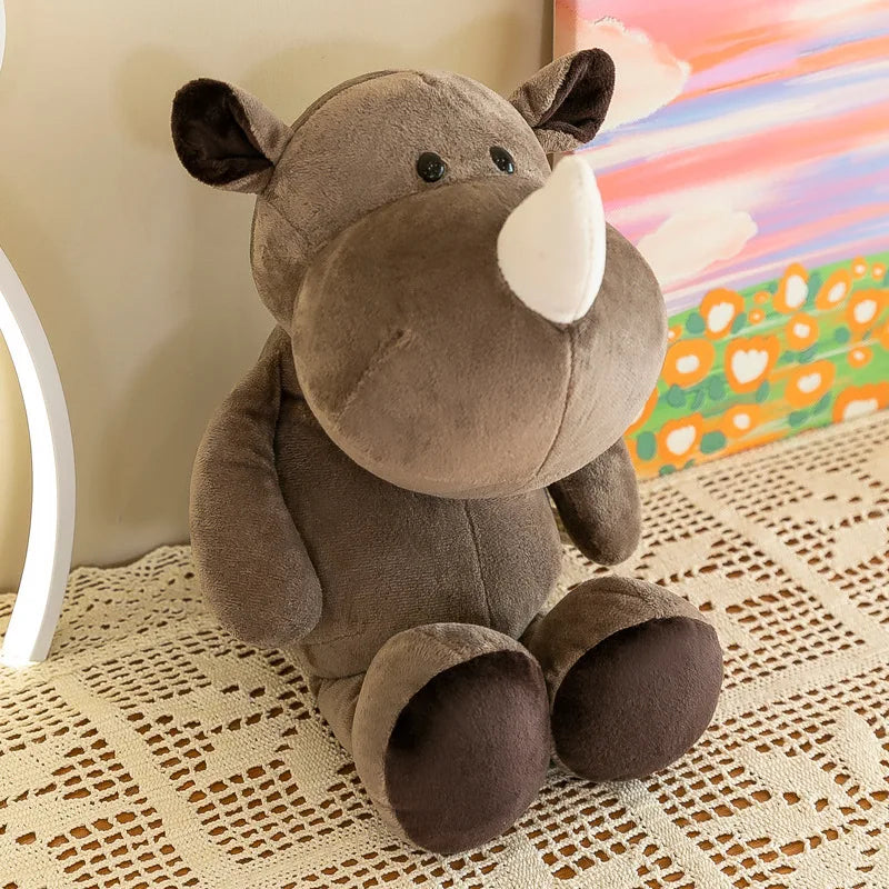 Un peluche de rinoceronte marrón con un cuerno blanco y ojos negros, hecho de material suave, se encuentra sobre un mantel de encaje, como parte de muñecos blandos de animales de la jungla.