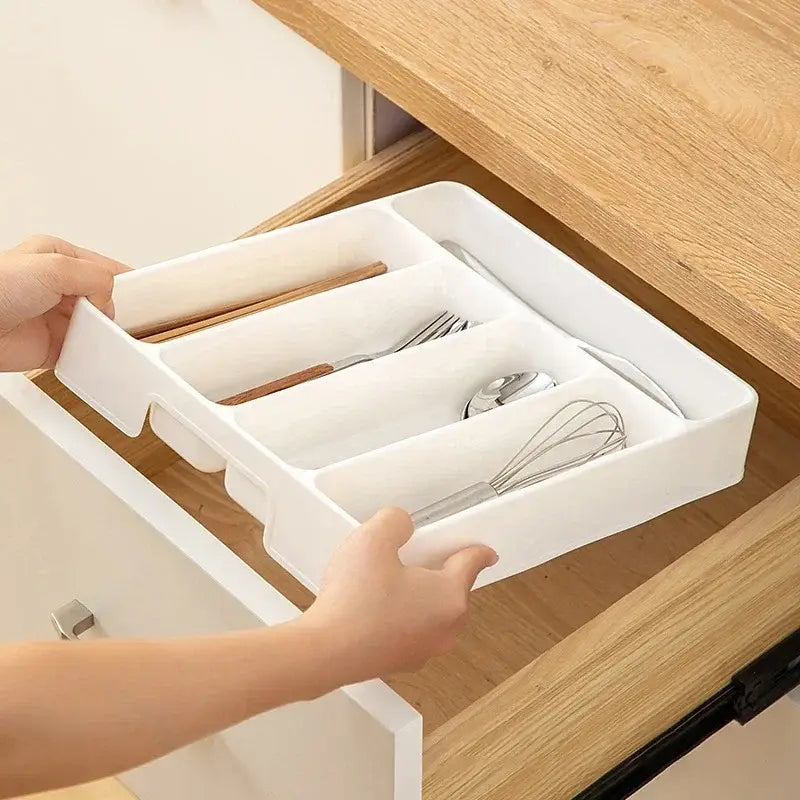Organisateur de tiroir à couverts en plastique blanc, avec des compartiments segmentés contenant des ustensiles et un fouet pour un rangement en cuisine.