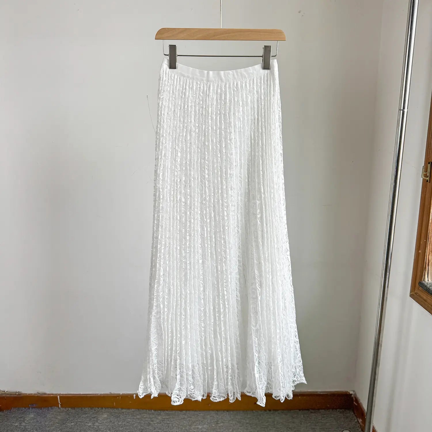 A white high waist pleated lace midi skirt hanging on a wooden hanger in y2k streetwear style.
