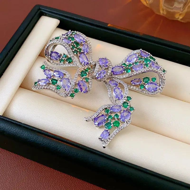 Eine funkelnde silberfarbene Zirkon-Schleifenbrosche im luxuriösen französischen Designschmuck, geschmückt mit oval geschliffenen lila Amethysten und smaragdgrünen Steinen.
