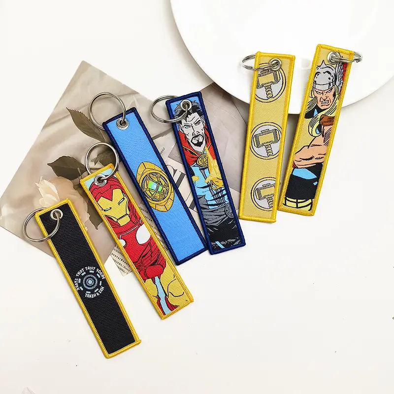 Superhero embroidered keychain set featuring iron man, doctor strange, thor, and the avengers logo in vibrant colors on fabric with metal rings for anime key lanyard use.