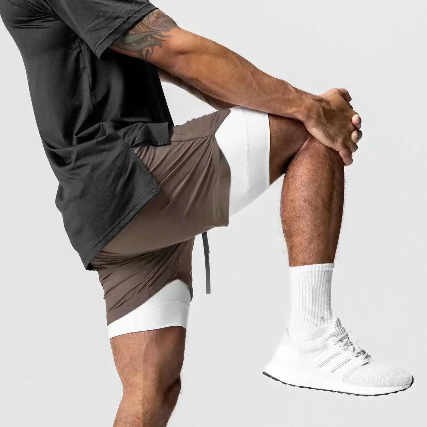 Hombres, pantalones cortos atléticos de dos capas marrones y blancos para gimnasio con cintura con cordón elástico y trabilla para la toalla que ofrece soporte para actividades de entrenamiento.