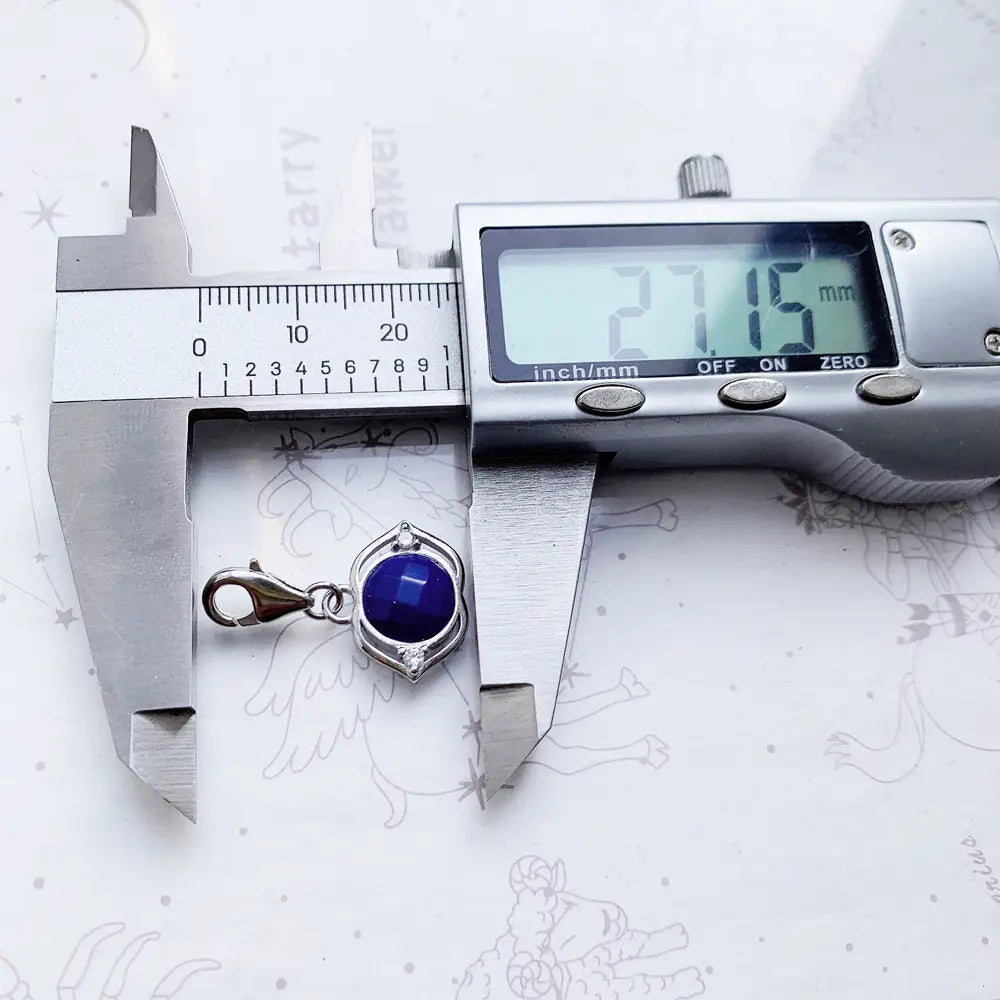 Colgante de encanto de plata de ley con acabado tono plateado que presenta una piedra preciosa facetada azul profundo engastada en un marco octagonal ornamentado, con un pequeño acento de diamante y un broche tipo langosta.