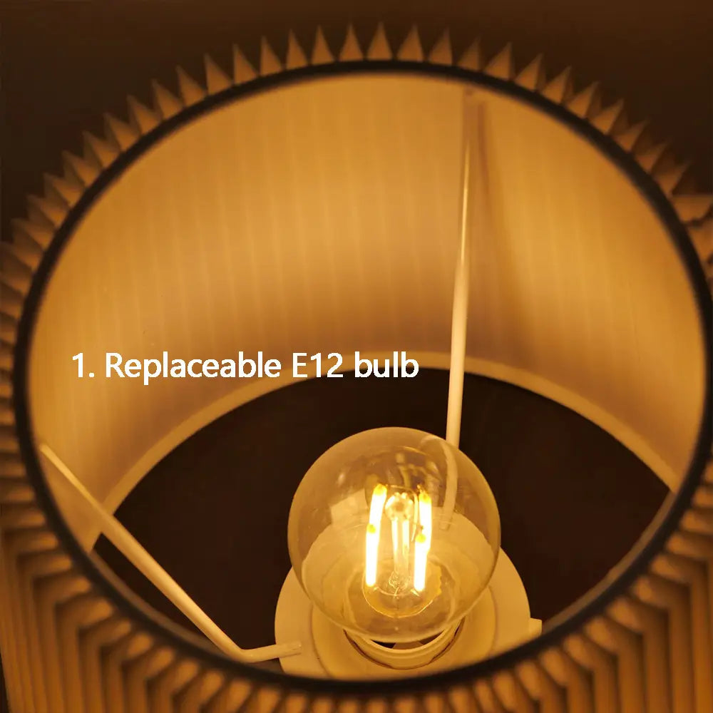 Eine warm leuchtende E12-Filament-Glühbirne mit einer klaren Glaskugel und sichtbaren inneren Spulen in einer plissierten Messing-Touch-Tischlampe, von vorn betrachtet