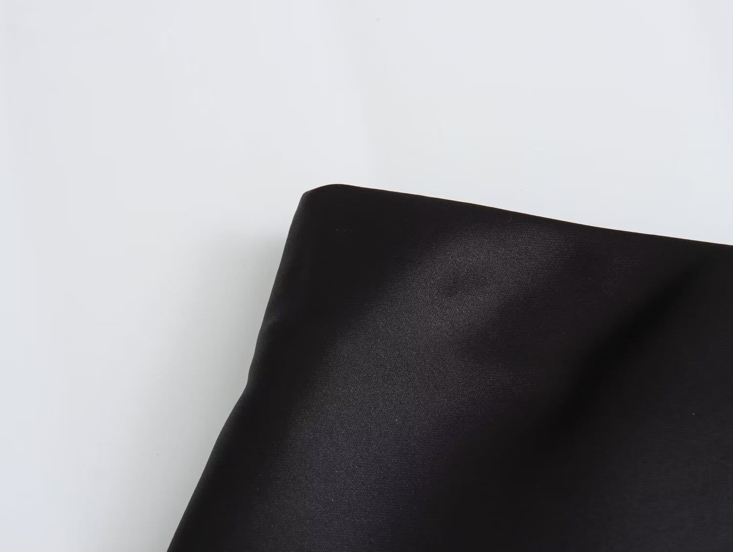 Taie d’oreiller en satin noir, finition lisse et brillante, complétant la jupe midi en satin à taille haute, élégante, en noir