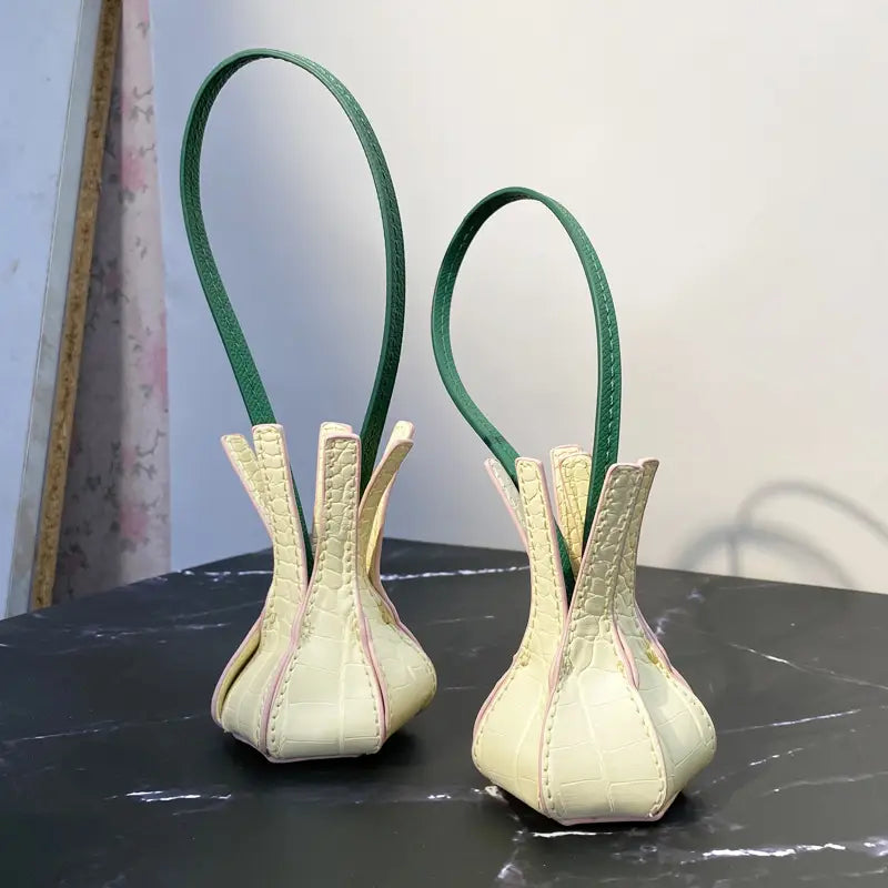 Un sac à main en cuir végétal gaufré façon crocodile, couleur crème, avec des poignées vertes, doté d’ornements et de charms de sac à main de créateur.