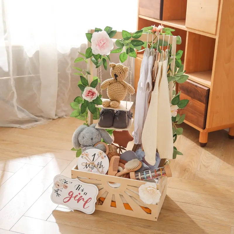 人工的なグリーンとピンクの花をあしらい、かぎ針編みのテディベア、赤ちゃんの衣類、保育園用品を収めた、木製のベビーストレージバスケットの収納、保育園の装飾。