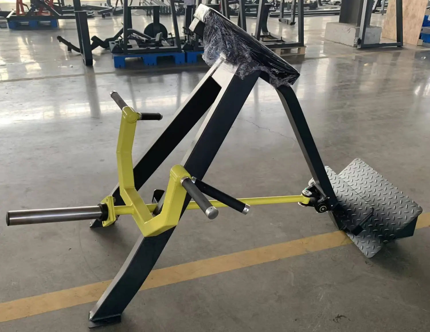 背面側から見た、テクスチャー加工されたフットプレートを備える、黒と黄色の角度付きレッグエクステンションを特徴とするプレートロード式着座ローイングマシン。