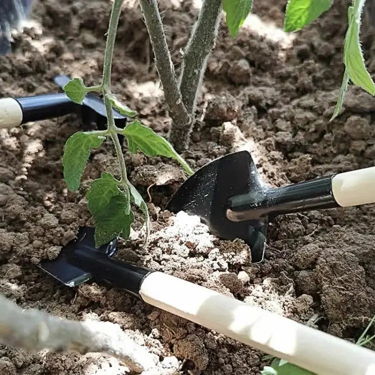 Black metal garden shovel with a light-colored wooden handle from a small gardening tools set positioned near young tomato plants in soil.