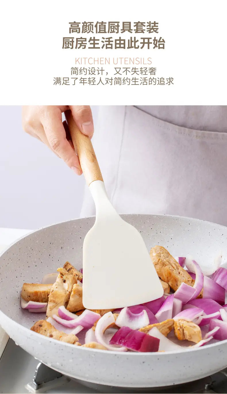 White silicone kitchen spatula with a light wood handle stirring chopped onions and chicken in a speckled gray pan.