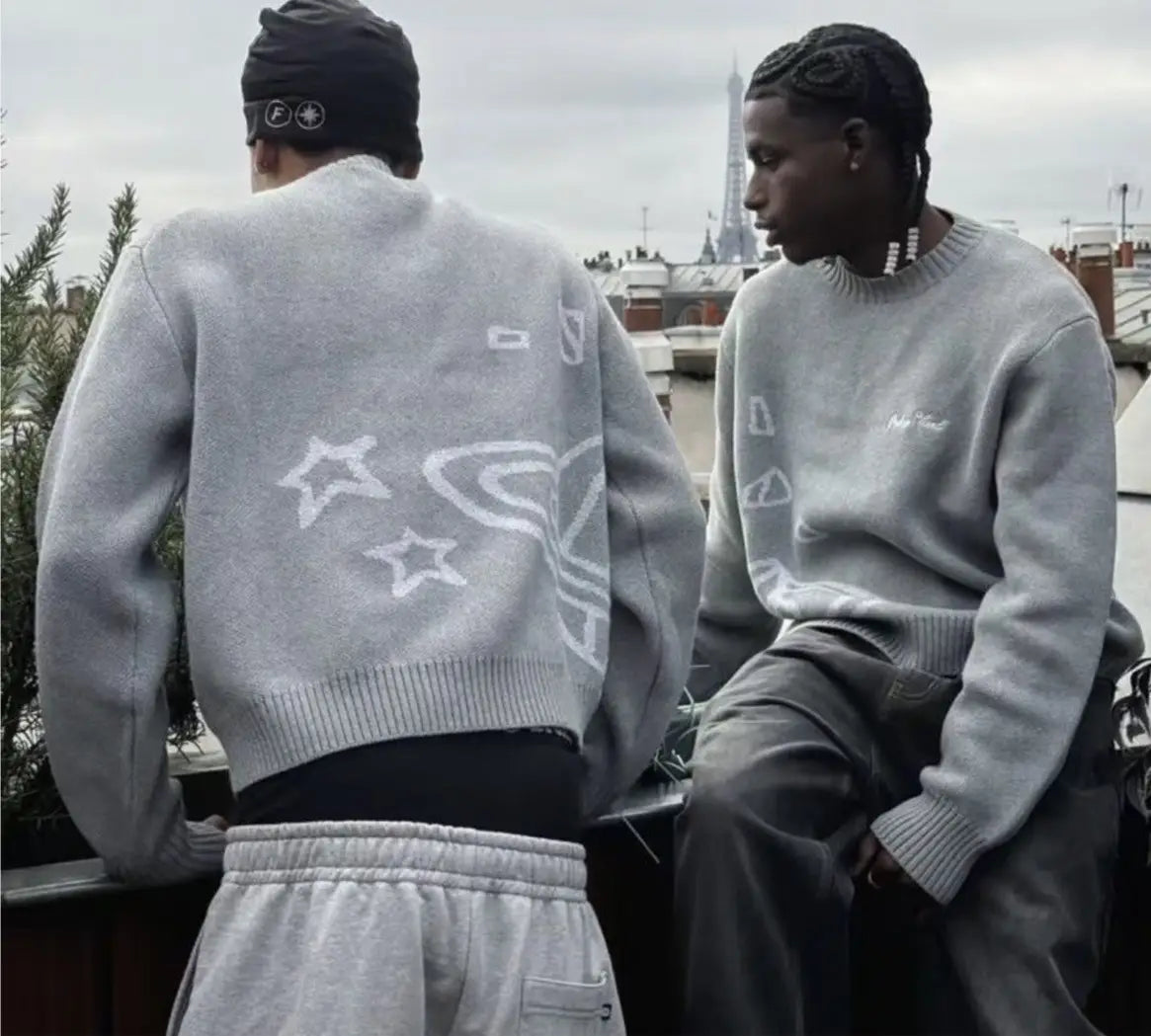 suéter de punto gris confeccionado con una tela suave que presenta estrellas bordadas en blanco y un diseño de planeta estilizado en la espalda, en el producto de suéter de punto con bordados y gráfico