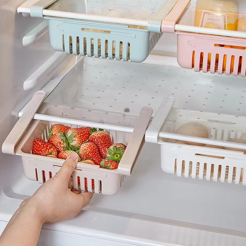 Beige plastic refrigerator drawer organizer with vertical slits and handle made of food-grade polypropylene holding fresh strawberries as part of an adjustable kitchen sink drain rack.
