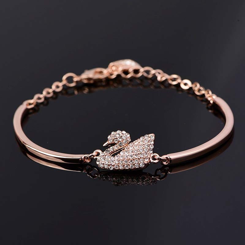Bracelet jonc à tonalité or rose, mettant en scène une breloque de cygne étincelante sertie de cristaux.