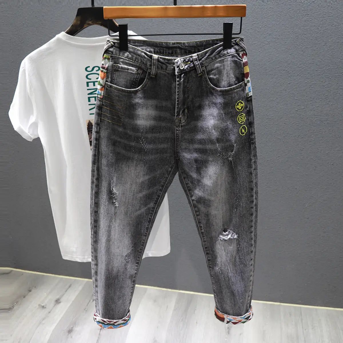 men slim fit stretch white denim jeans featuring dark gray distressed fabric with colorful embroidered patches and a patterned cuff