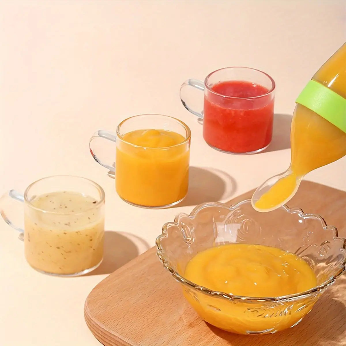 Eine klare Glaskanne mit hellem grünem Silikon-Griff, die Orangensaft in eine verzierte Glasschale gießt, als Teil eines Silikon-Babynahrungstrinkfläschchen- und Schnuller-Sets.