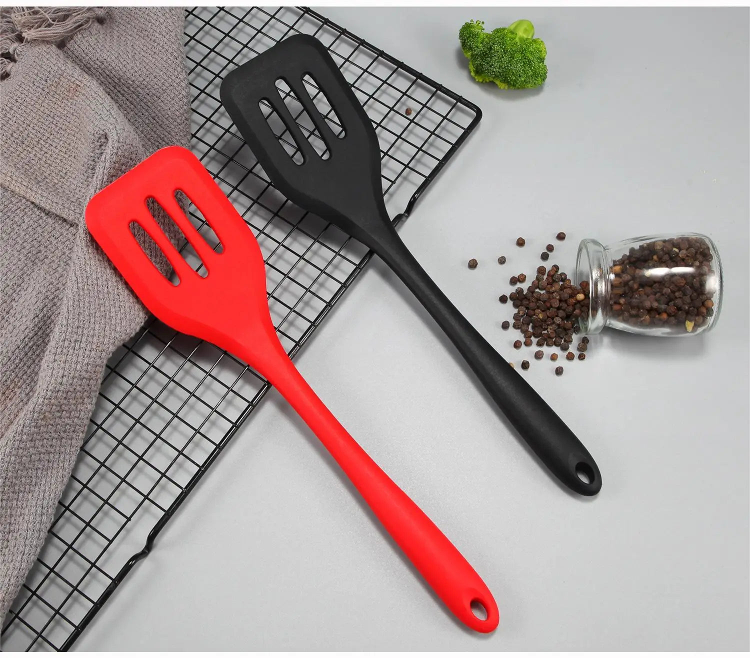 Rotes und schwarzes Küchenwender-Set aus Silikon mit geschlitzten Köpfen, die auf einem Drahtgestell ruhen, gefertigt aus hitzebeständigem Silikonmaterial.