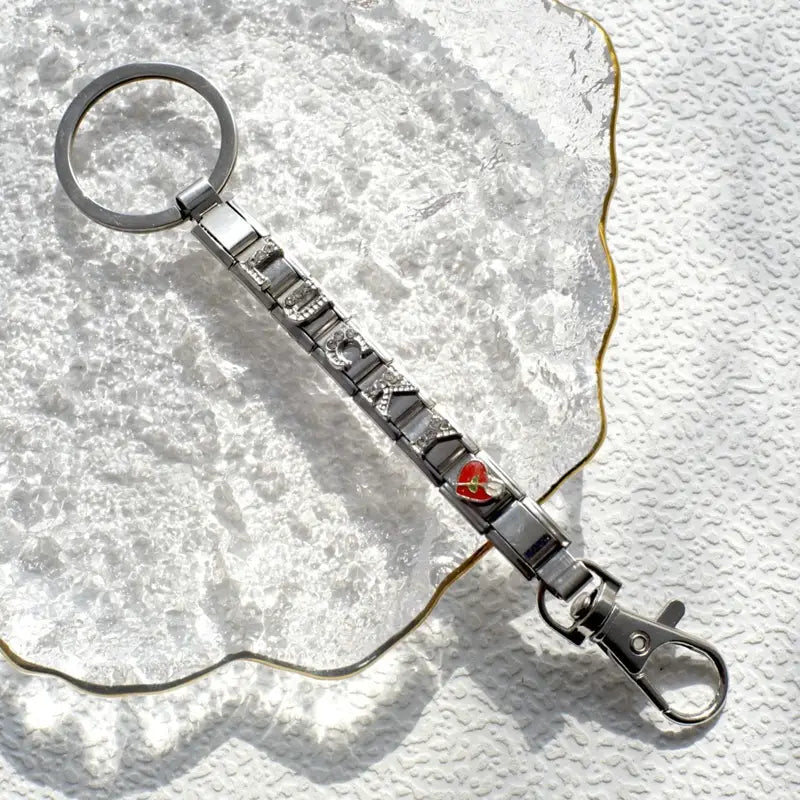 Llavero con dije de eslabones italianos con acabado plateado, con eslabones metálicos entrelazados que forman la frase «I love» y un dije de corazón rojo; incluye un broche tipo langosta para uso personalizado en bricolaje.