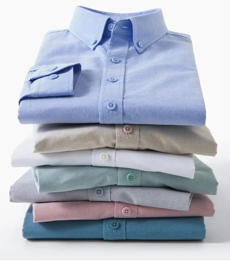 Pila de camisas abotonadas de algodón suave y con pliegues ordenados, en colores pastel, que incluye una camisa Oxford de algodón color azul claro, corte slim fit, para hombre.
