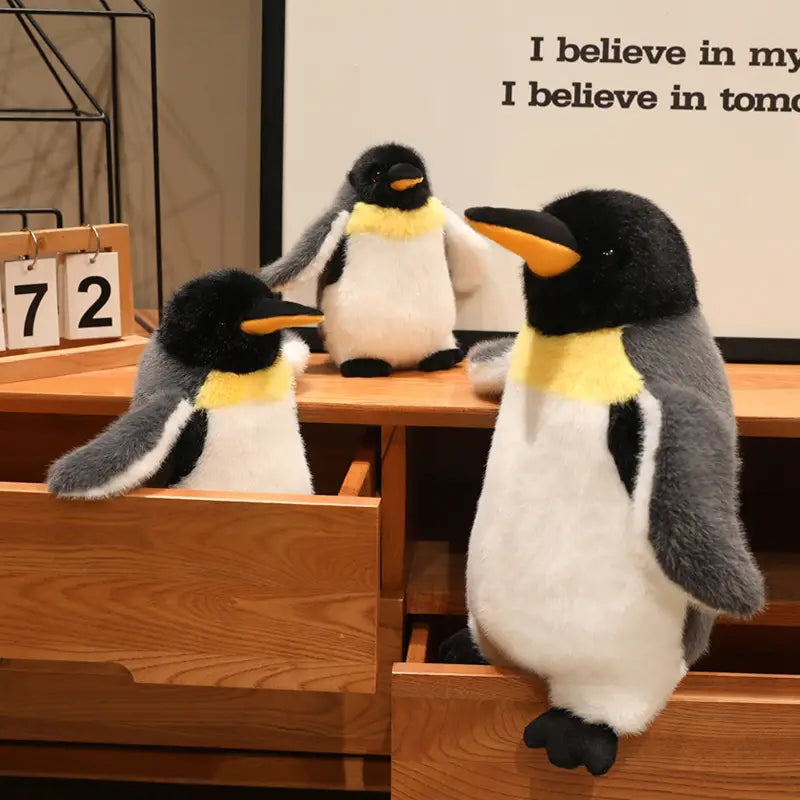 three plush penguin stuffed animal soft toys with black and white bodies yellow neck bands and orange beaks made of soft material for cuddling and decoration
