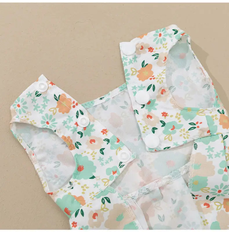 A delicate floral-patterned fabric diaper cover with soft pastel hues and white snap closures as part of the floral dog princess dress with bow.