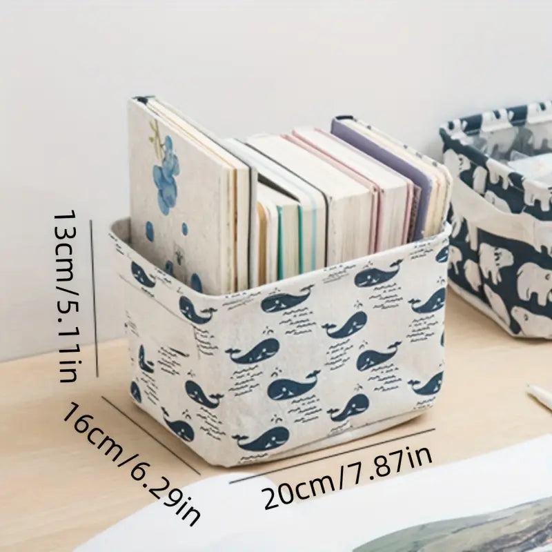 Panier de rangement pliable en tissu blanc avec un motif de baleine bleu marine et d’écriture, permettant de maintenir des cahiers empilés comme boîte de rangement pour une organisation optimale.