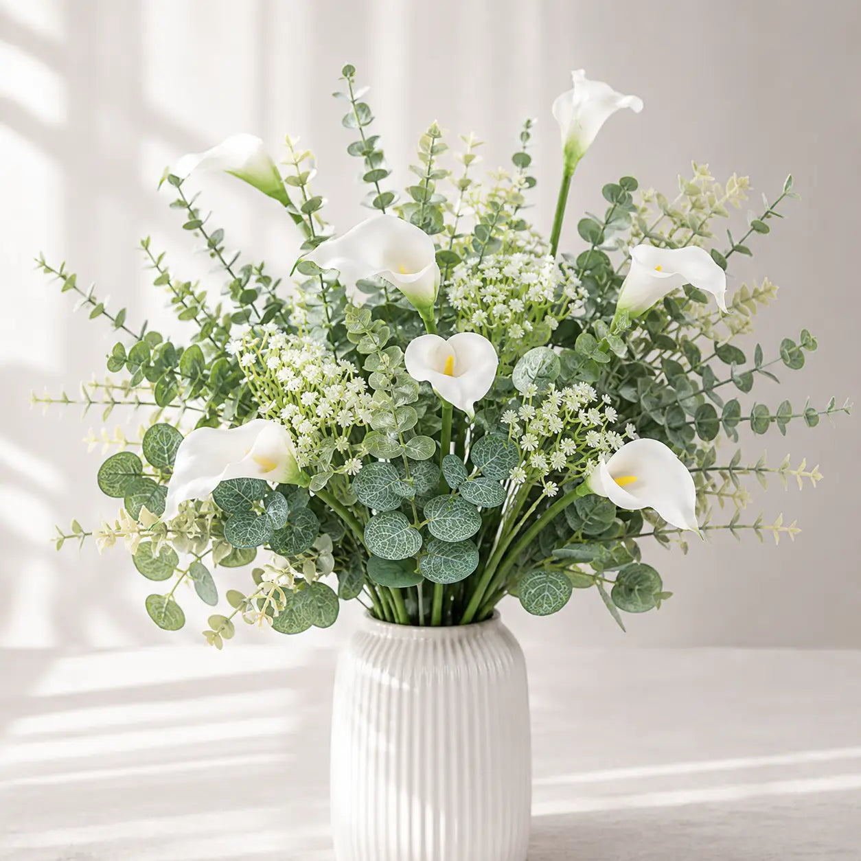A white ceramic vase with vertical ridges holds a lush arrangement of artificial mixed flowers featuring calla lilies and eucalyptus from the mixed flowers 48pcs wedding bouquet set.
