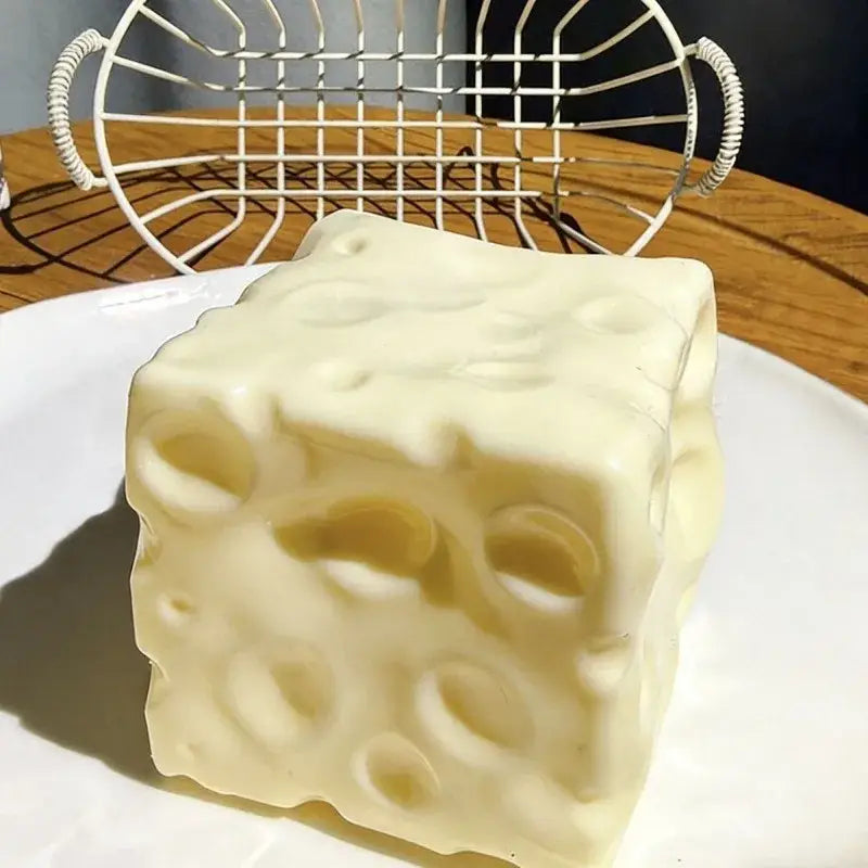 Cream-colored cube-shaped cheese block stress relief squeeze toy with a realistic swiss cheese texture and pattern.