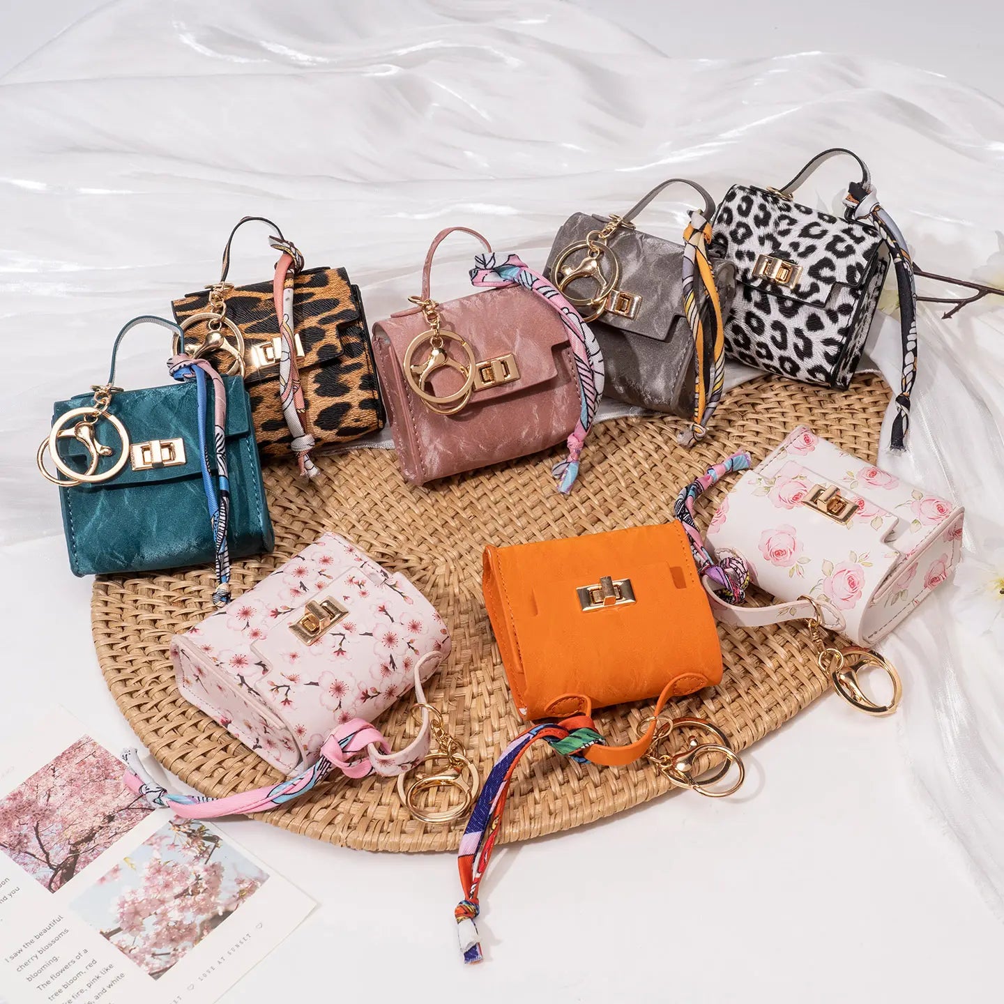 A collection of colorful miniature handbag keychains with gold-tone hardware and patterned or solid leather-like exteriors featuring silk scarves.