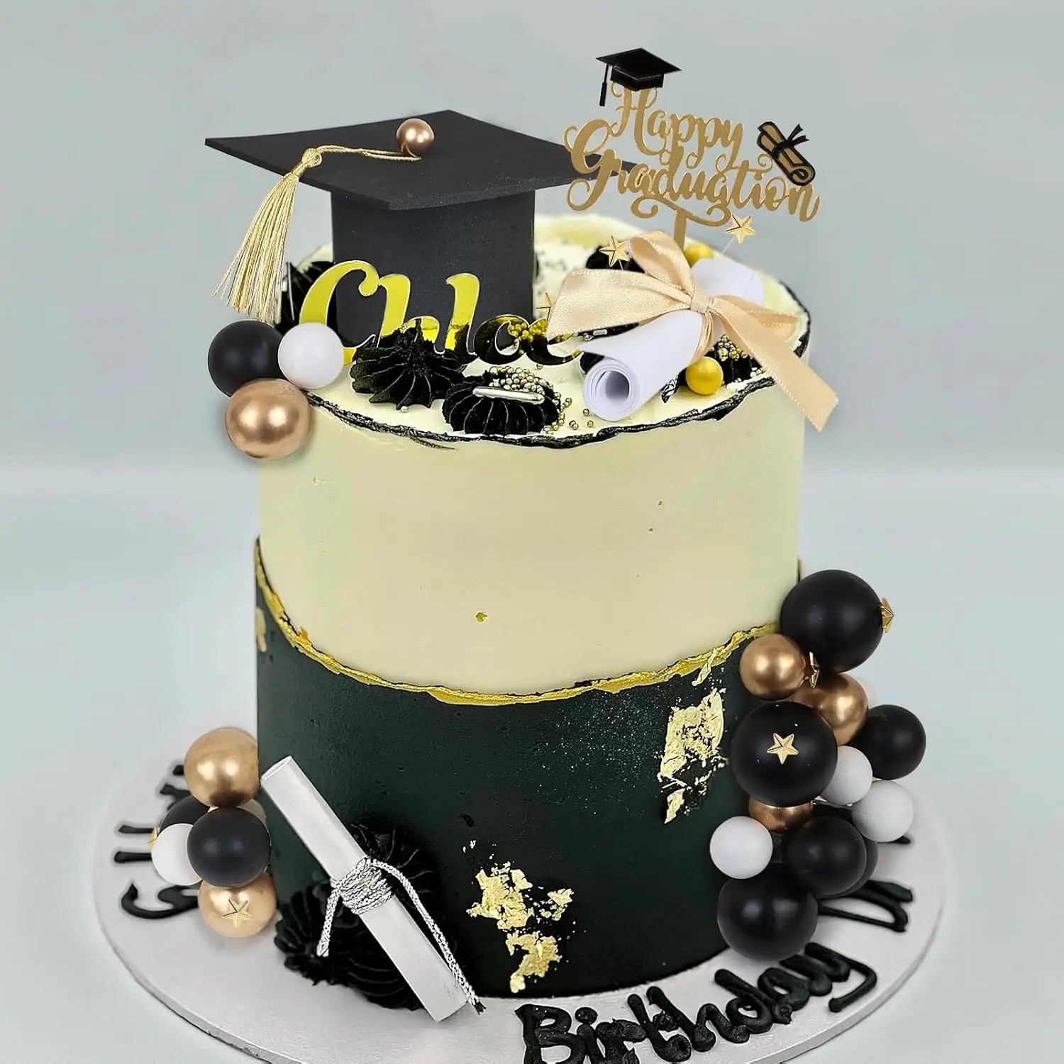 A two-tiered graduation cake topper set for 2026 senior party featuring a black and gold cake with edible decorations including a miniature cap diploma scrolls and metallic spheres.