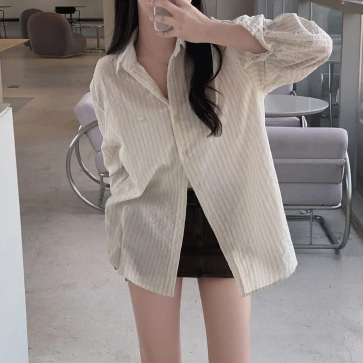 A loose-fitting off-white striped long sleeve button down shirt with a subtle vertical striped pattern and slightly textured fabric offering a versatile style and standard thickness.