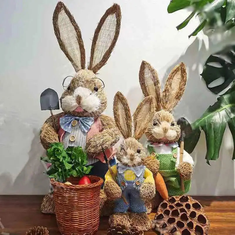 Three rustic woven 35cm straw Easter rabbit figurines dressed in miniature clothing and holding gardening tools.