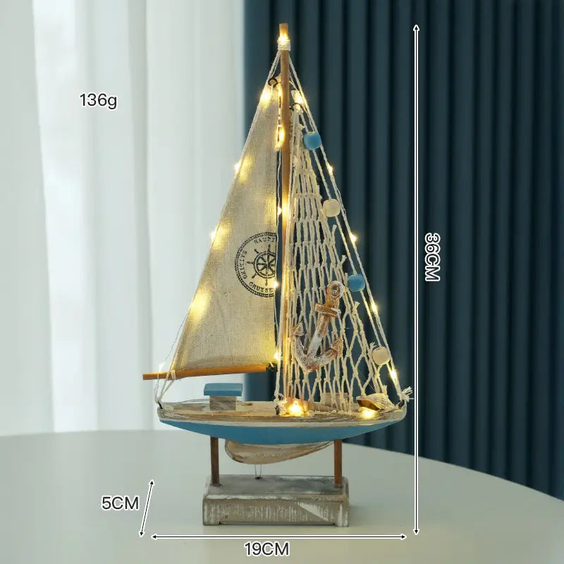 Deko im mediterranen Stil mit einer hölzernen LED-Segelboot-Dekoration für das Zuhause: Sie weist ein dekoratives Modell-Segelboot mit einer beigen Segelleinwand, einem blauen Rumpf, einem hölzernen Mast, Lichterketten und maritimen Details auf.