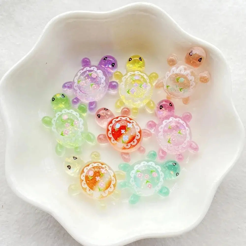 Colorful translucent resin turtle flatback charms with delicate floral patterns and lace-like detailing on their shells in a 10 pack.