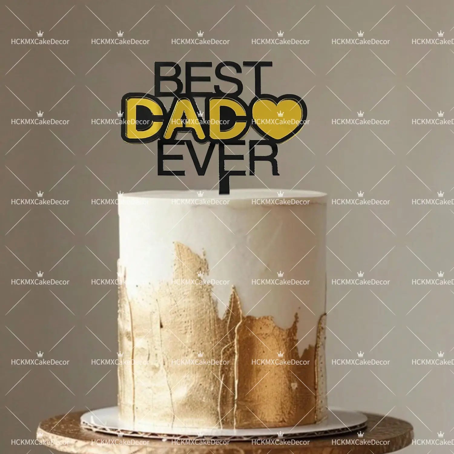 A sleek white cake with gold leaf accents topped with a bold black and yellow best dad ever acrylic cake topper set for Father’s Day.