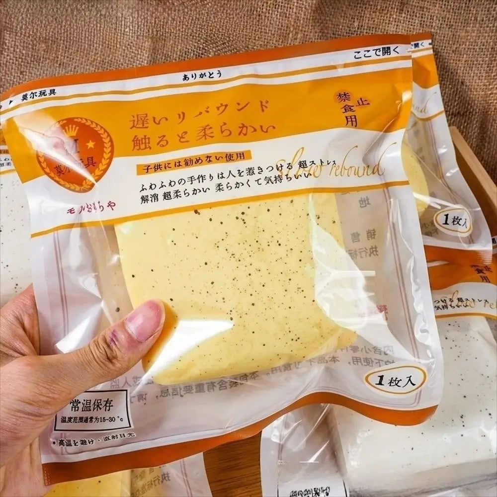 ein hellgelber gesprenkelter Schwammkuchen in einer transparenten Plastikhülle mit orangefarbener und weißer Beschriftung, der neben einem Polyester-Acryl-Winterschal ausgestellt ist.