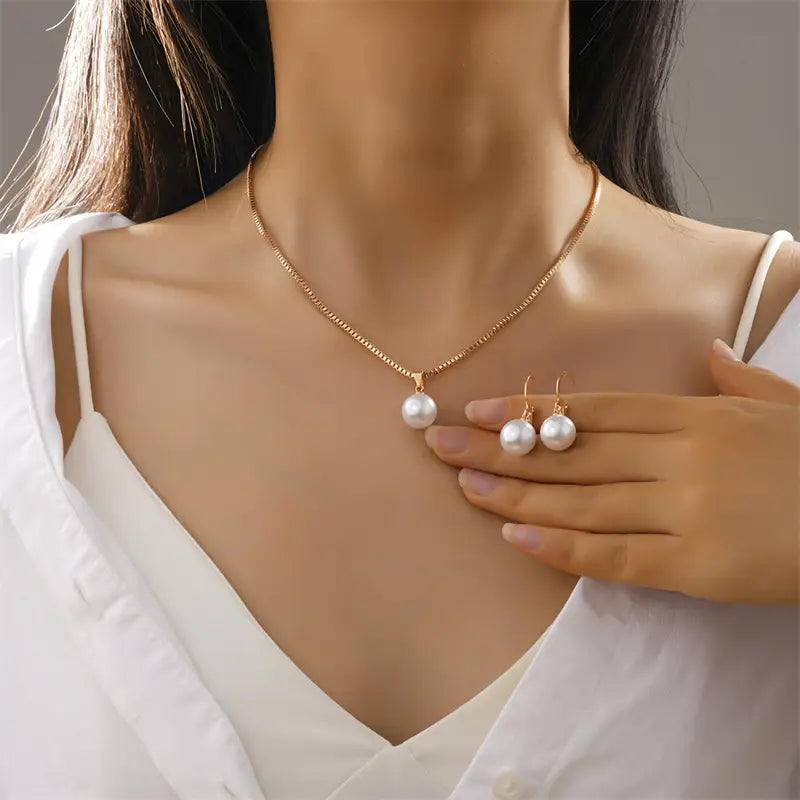 A delicate gold chain necklace and matching earrings featuring a single lustrous white pearl pendant in a pearl jewelry set gold necklace and earrings.