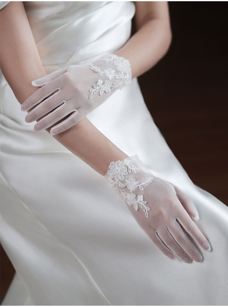 white lace bridal gloves in tulle material with delicate floral embroidery along the wrist designed for wedding use.